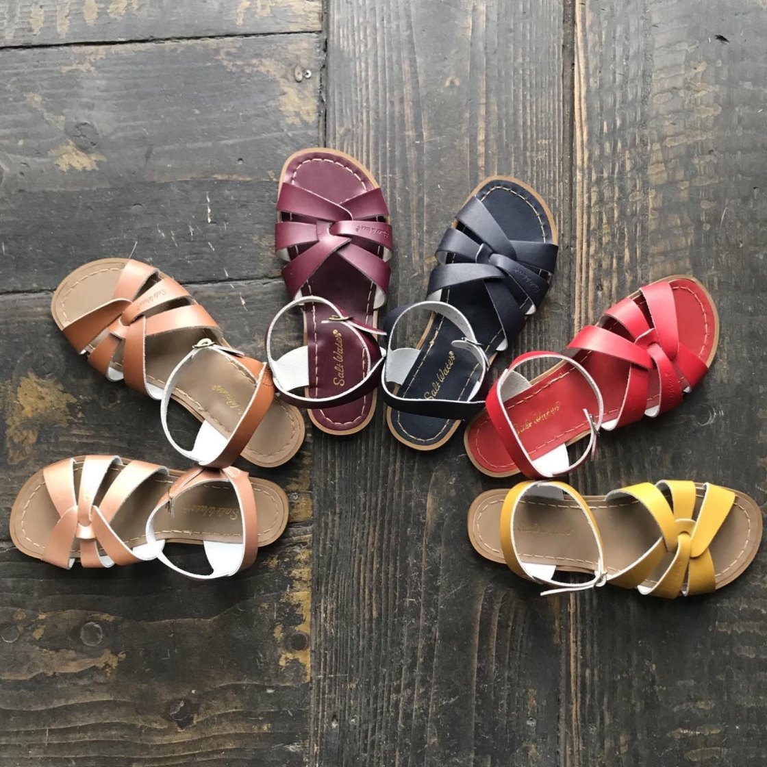 An image of 5 different coloured sandals in a fan formation; from left to right the sandal colours are latte, tan, claret red, navy blue, red and mustard yellow. 