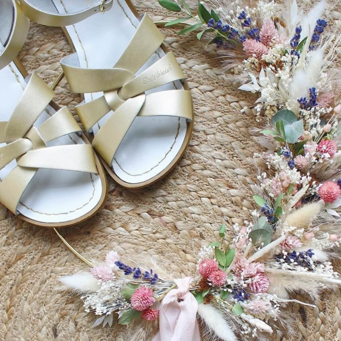 a pair of gold sandals on a woven mat surrounded by a garland of dried flowers