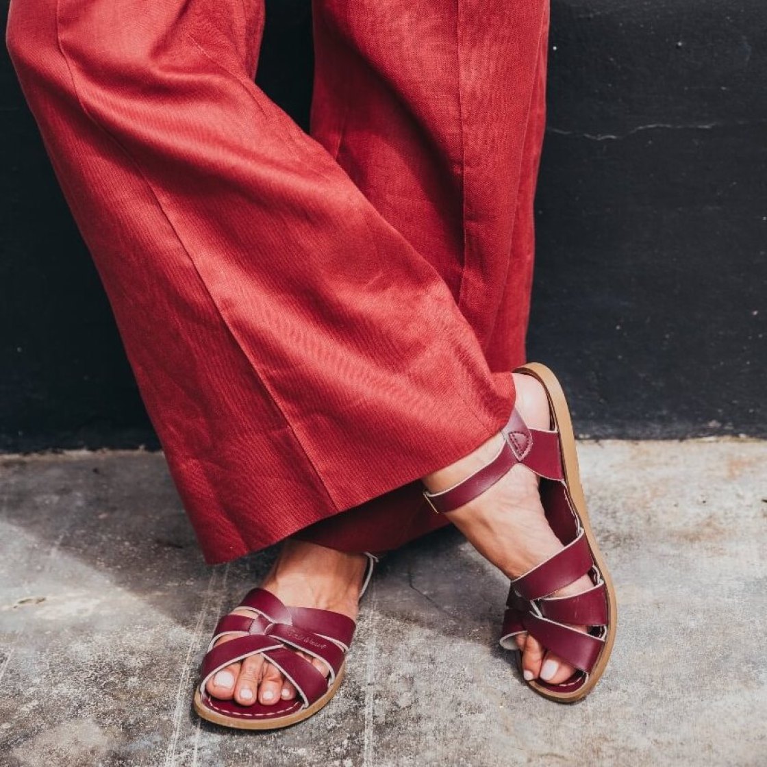 a women in a red, wide linen trouser, is wearing a claret coloured red women flat sandal.